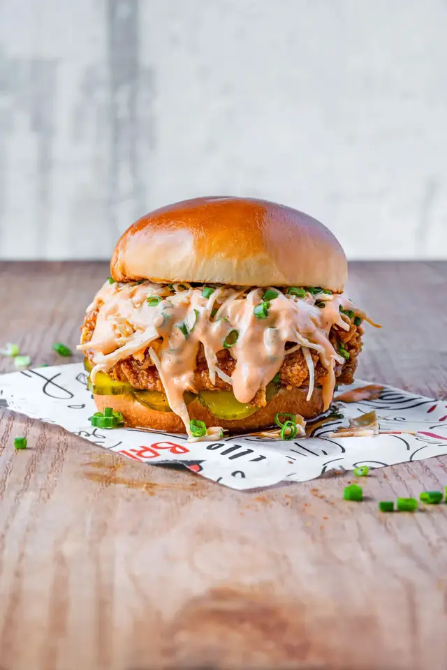 A crispy chicken burger on branded paper on a wooden board