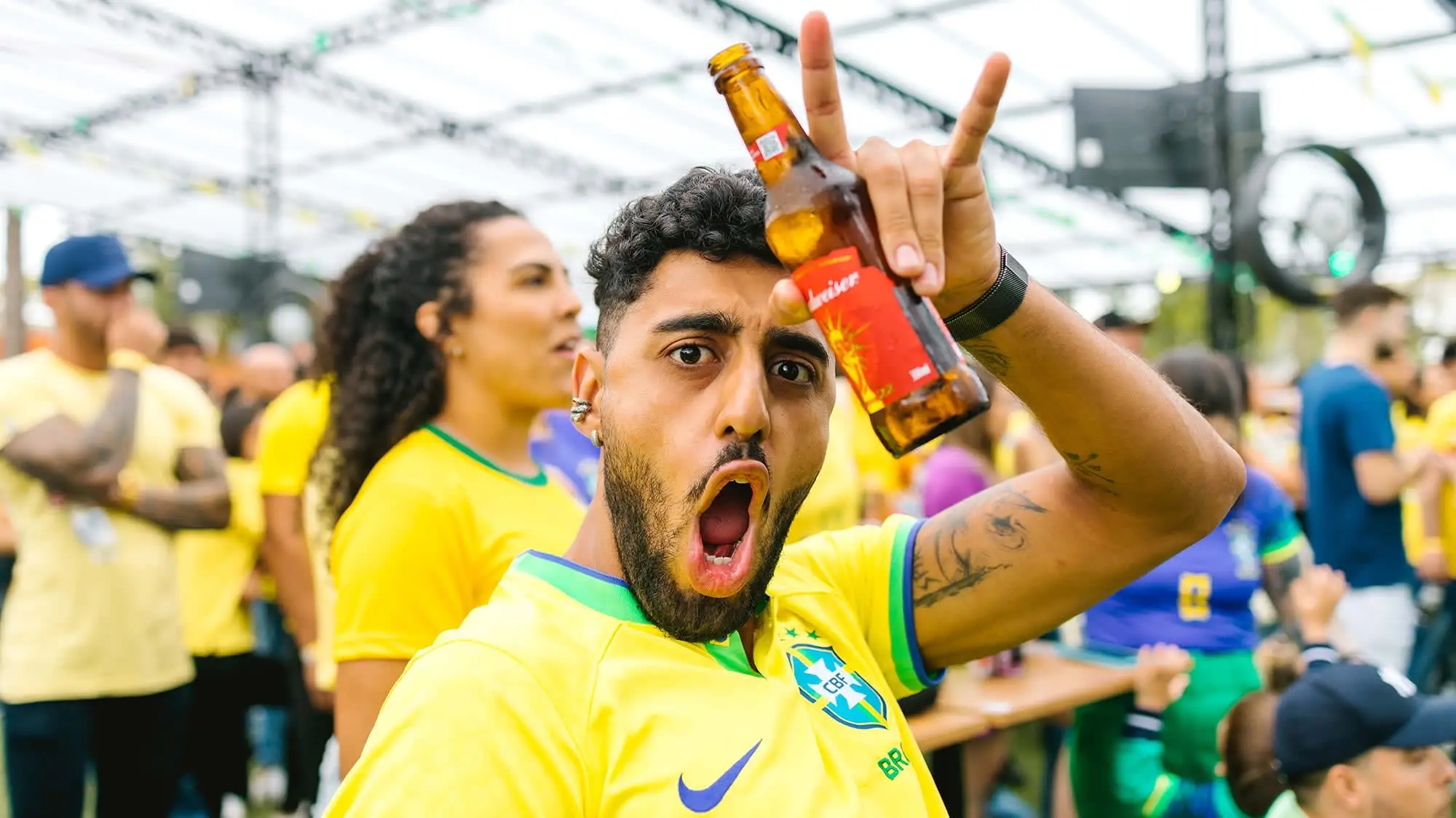 A avid soccer fan cheering and drinking beer while facing the camera.