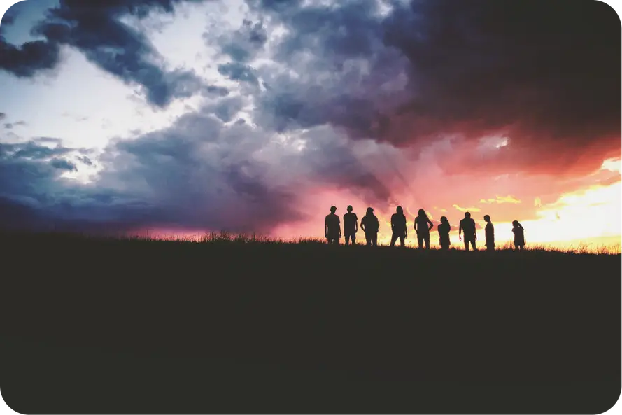 group hiking with hikers silhouettes backdropped by the sunset on the horizon