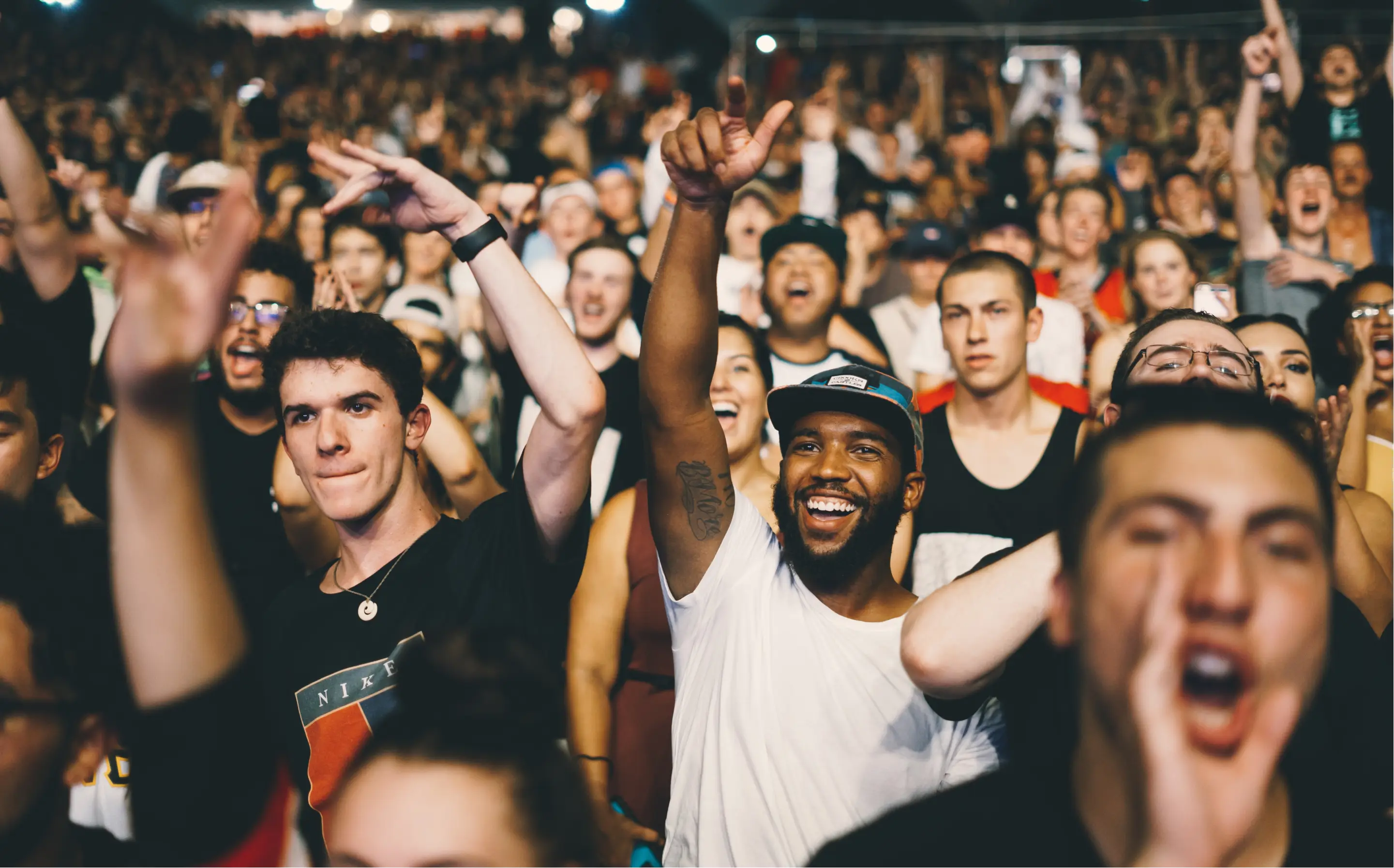 A group of happy people in a crowd cheering at a music event.